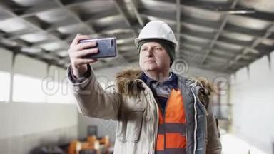 一个戴着安全帽、穿着工作服的人正站在机库的中央，用手机在机库里拍照